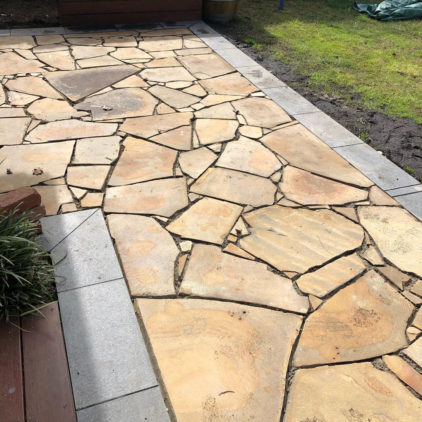 Sandy-coloured crazy paving patio with grey edging beside a lawn