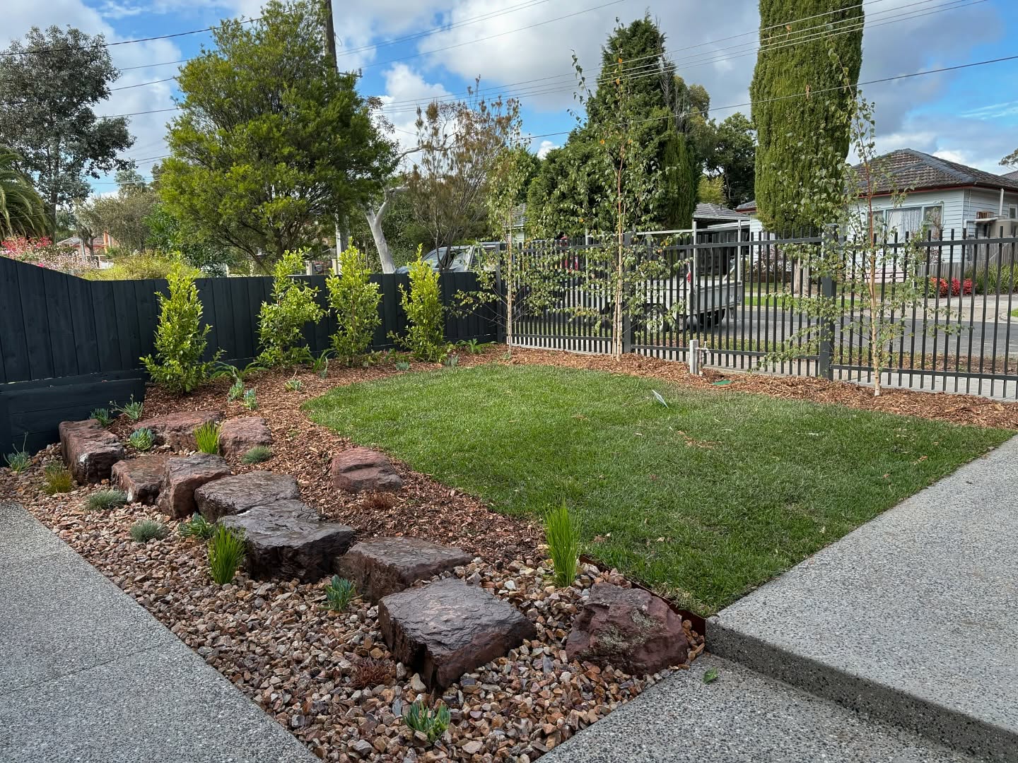 Front garden with feature rocks, pebbles and lawn beside an exposed aggregate path