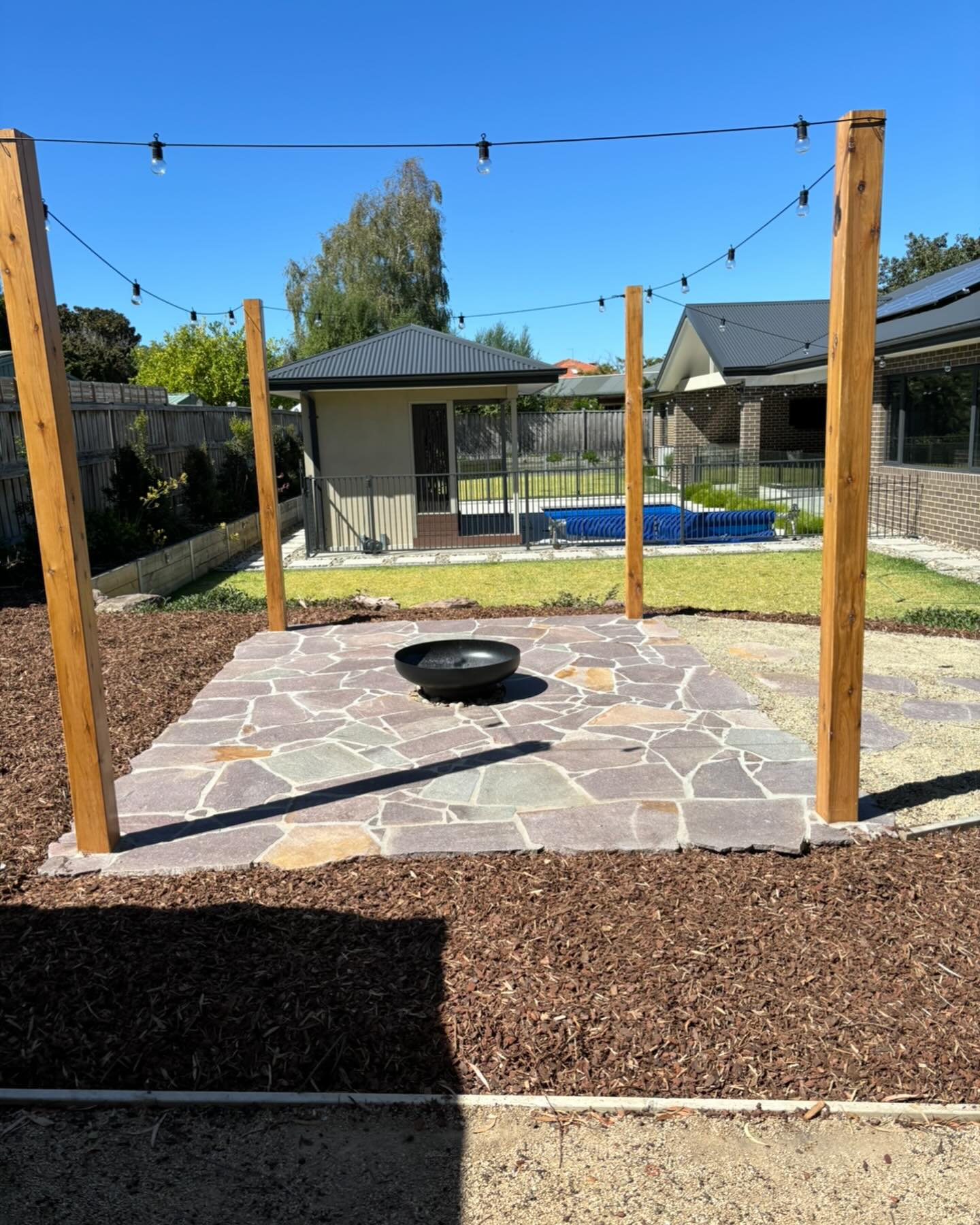 Crazy paving fire pit area framed by timber posts with festoon lights