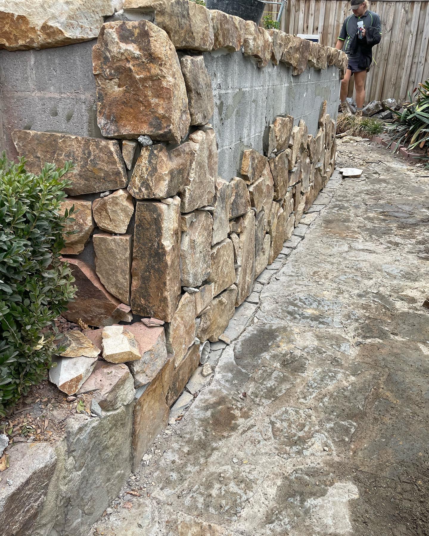 Stacked rock retaining wall alongside a paved side path