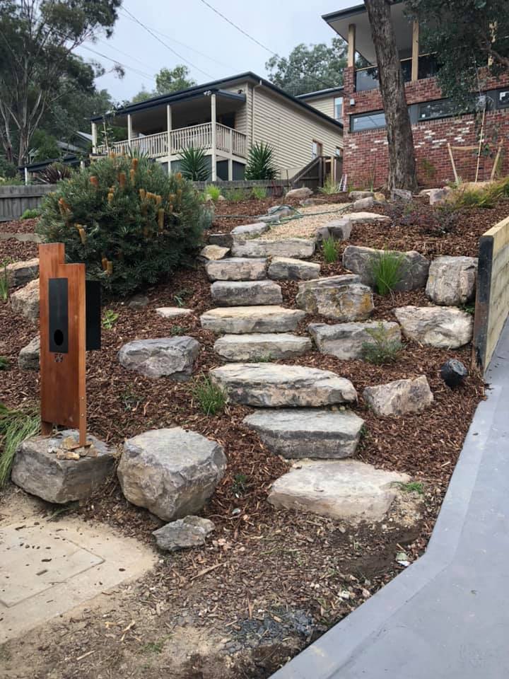 Rock steps winding up a mulched garden slope in front of a house
