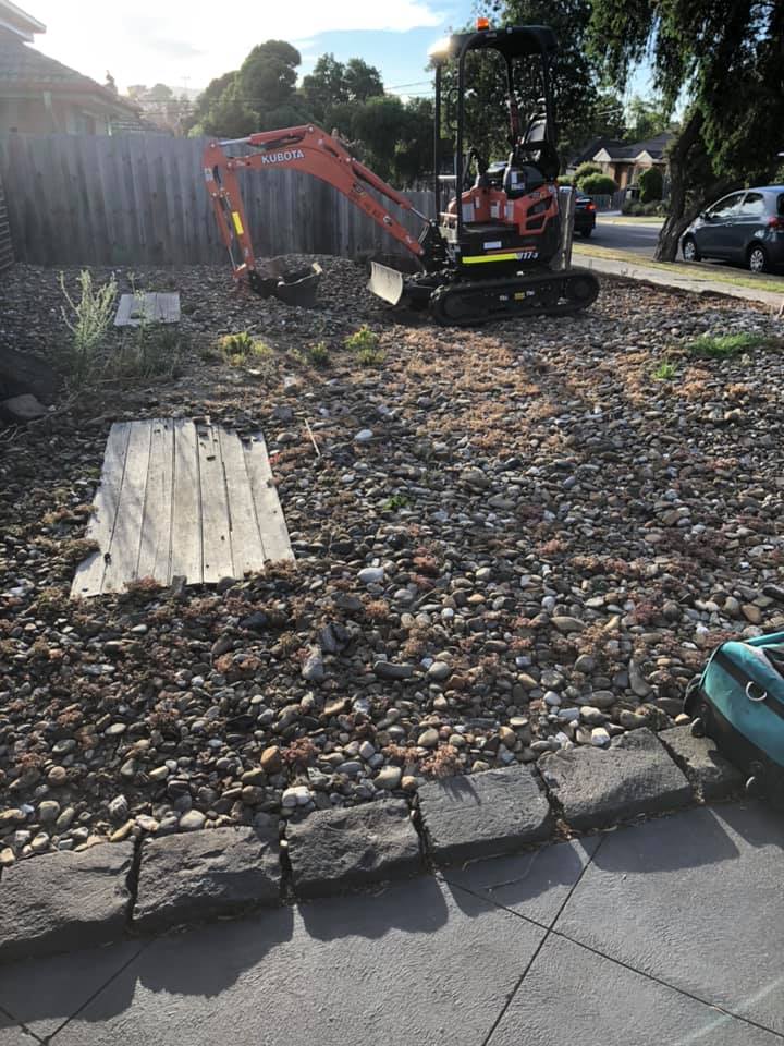 Mini excavator working on a front garden bed of river pebbles with stone edging
